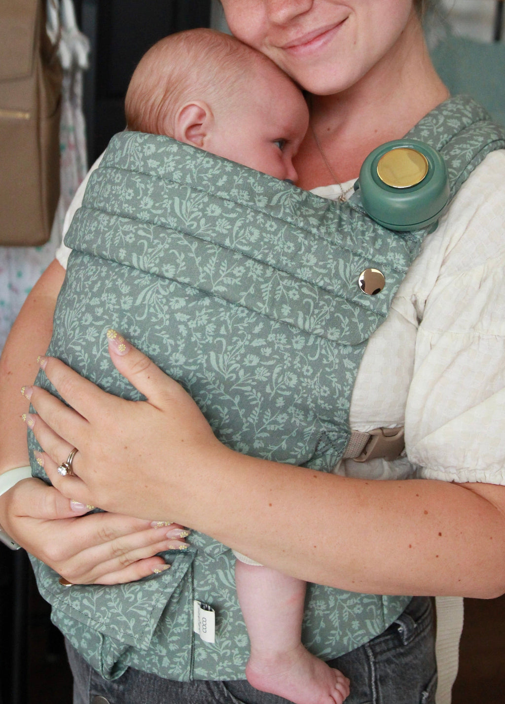 Woman holding a baby in a green baby carrier in a clothing store.